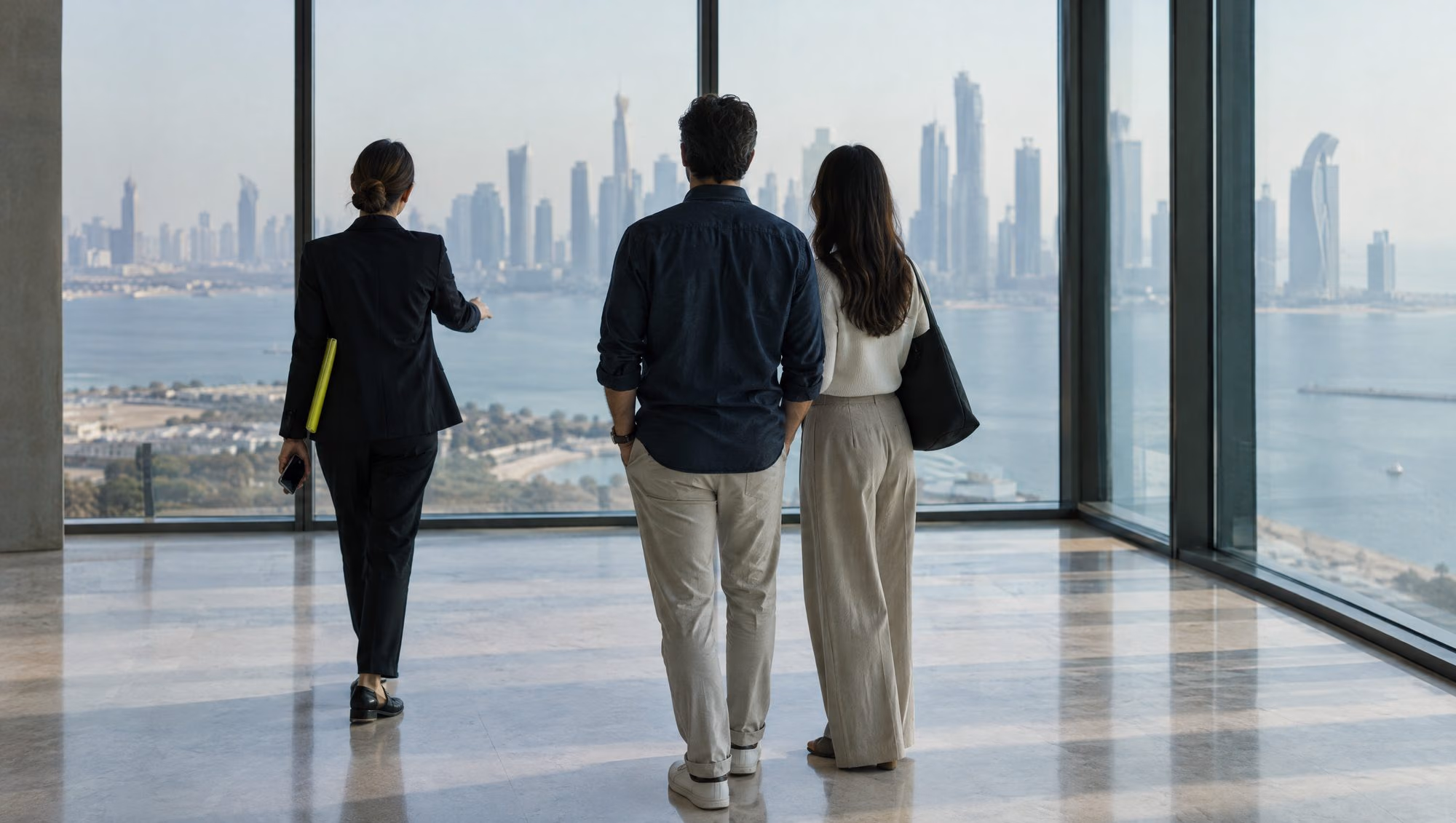 A property agent showing an empty apartment with a view of a city skyline and the sea to a couple