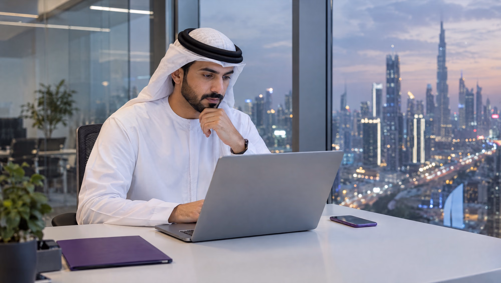 A sales manager reading the day's visit reports on a laptop in an office at dusk, the city lights outside