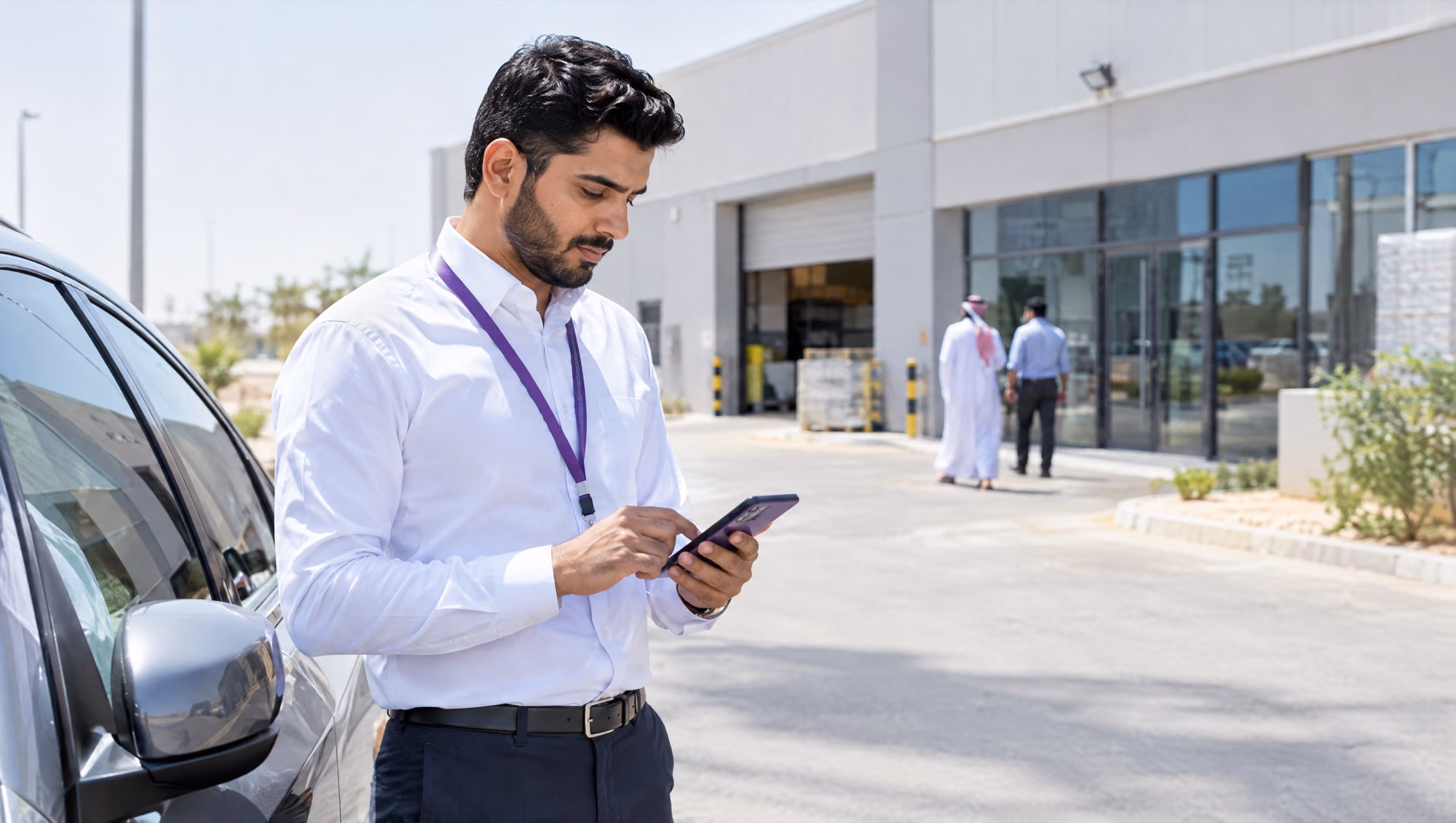 A sales rep filling in a visit report on his phone beside his car, outside a customer's light-industrial unit