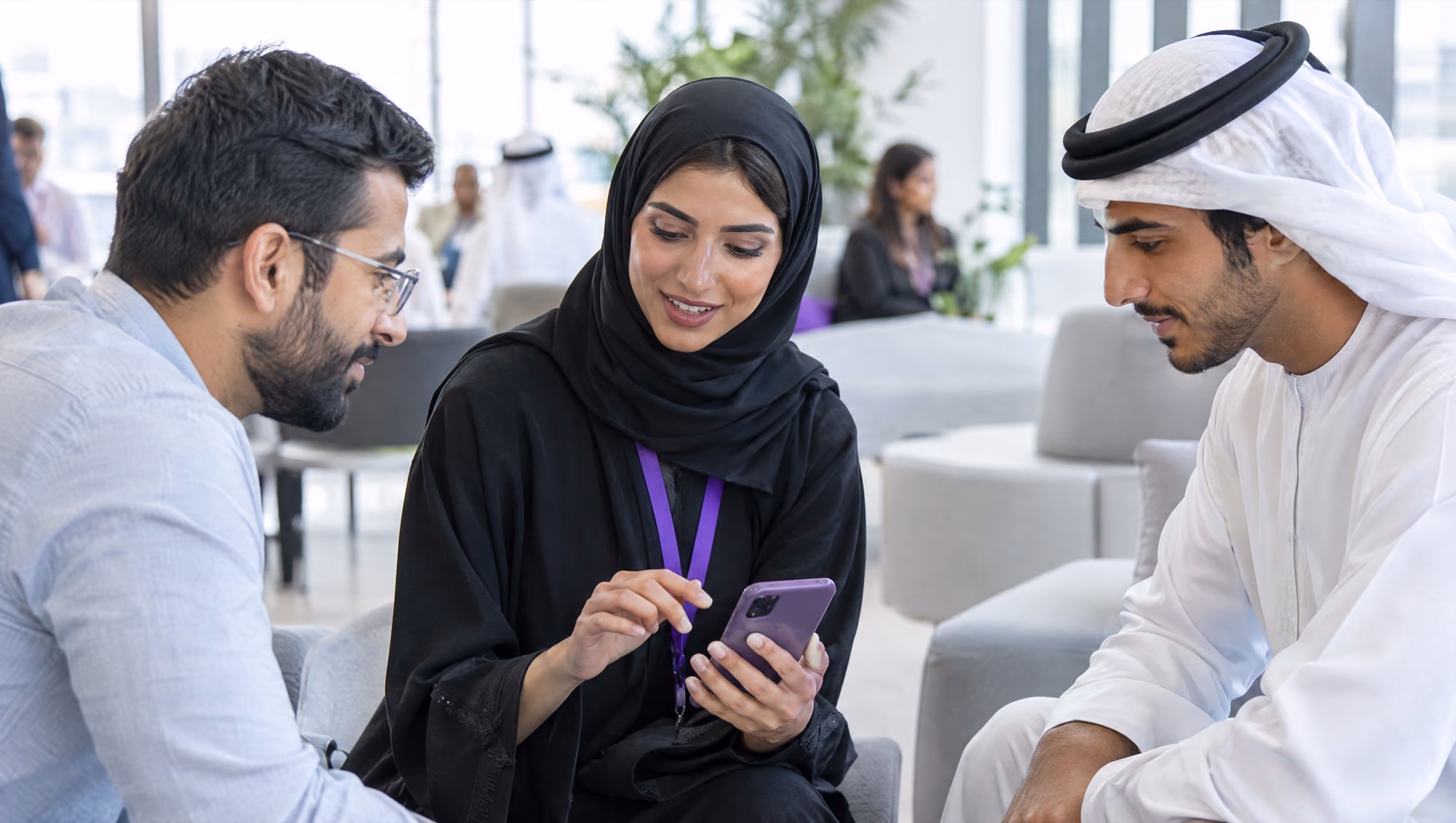 A founder showing her product on a phone to two people at a meetup in a bright co-working space