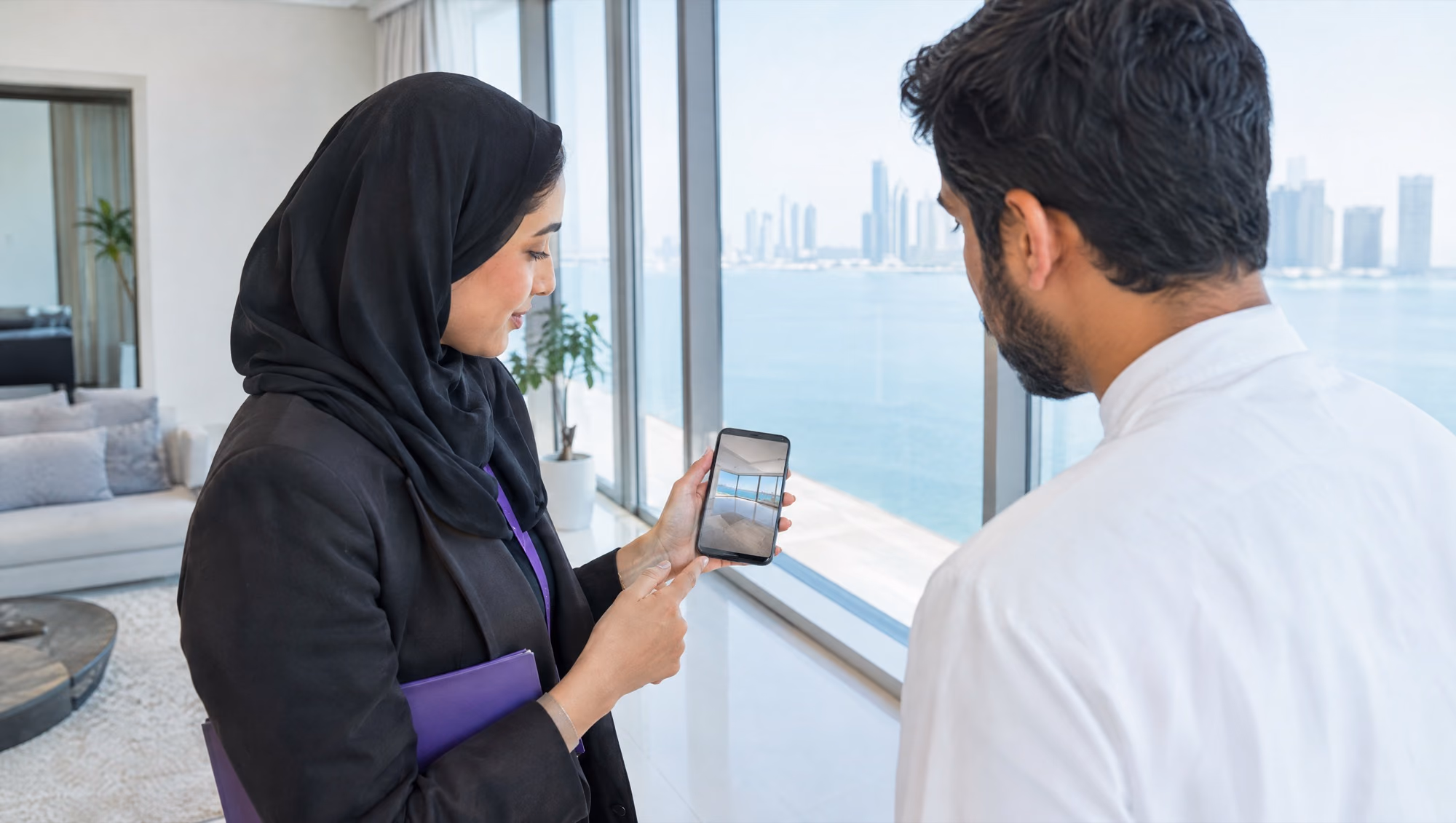 A real estate agent with a phone showing an apartment with a sea view to a client